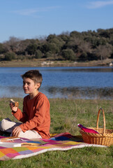Boy eating a sandwich while picnicking at a lake in an orange t-shirt
