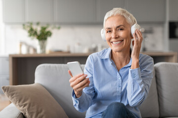 Senior Woman Listens Music On Headphones And Phone At Home © Prostock-studio
