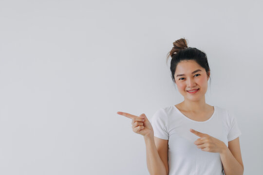 Asian Thai woman pointing finger at empty space, recommend something good value, showing idea information at blank wall, standing isolated on white background.