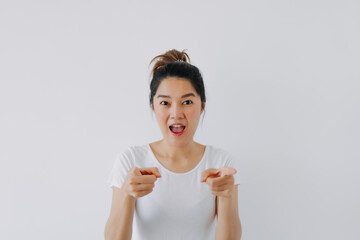 Asian Thai woman wow surprised face and pointing fingers to camera, recommending something, standing isolated over white background wall.