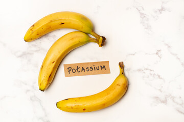 Plátanos junto a un cartel con la palabra potasio sobre un fondo de mármol blanco texturado....