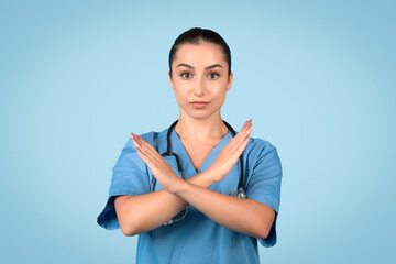 Serious european woman nurse in blue uniform crossing her arms to form an X sign, symbolizing...