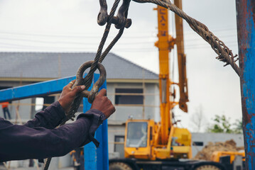 Man hand pulling metal sling of crane to lift cement platform at construction site.