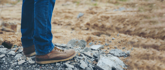 Legs of Lonely man wearing jeans and leather boots walking along the path strewn with rocks. Travel...