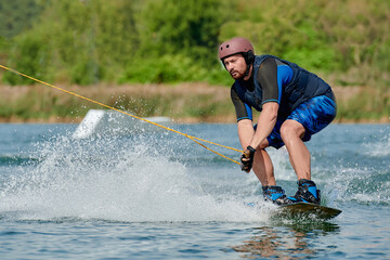 a man on a wakeboard holds onto a winch and sits down before performing a trick