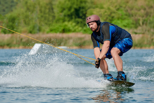 a man on a wakeboard holds onto a winch and sits down before performing a trick