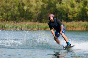 a male wakeboarder holds onto a winch and rides through the water with splashes