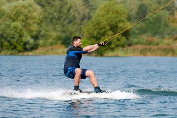 a male wakeboarder rides on the water squatting holding on to a winch