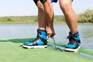 a man with tattoos ties his wakeboarding shoes on the background of a pond