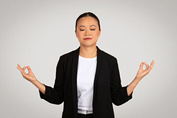 Serene Asian businesswoman in a black jacket with eyes closed practicing mindfulness or meditation