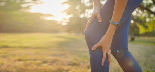 woman with knee pain in evening park. hold her sports injured knee. Low section of sports female...