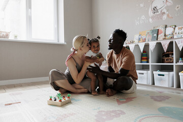 Happy multiracial parents playing with their toddler daughter in nursery.