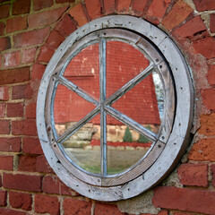 Reflection of red old mill in round window: square photo, red brick.