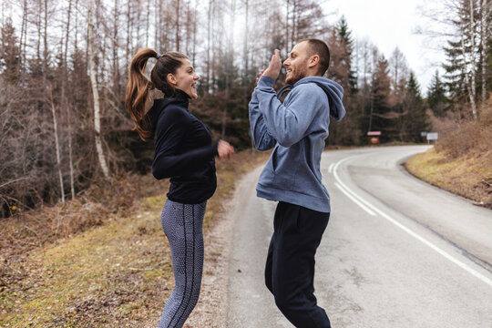 Happy Caucasian runners giving high five during running in nature on cold weather. Shot of a sporty young couple high fiving while exercising outdoors.