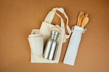Fototapeta na wymiar Devices for drinks. Zero waste concept. A tin bottle for water with beige bag and wooden cutlery on a brown background. Flat lay