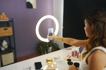 Teenage girl attaching smartphone to ring light to film her daily makeup
