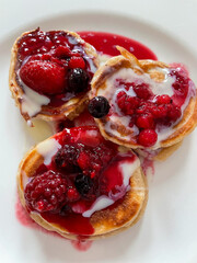 Homemade pancakes with fresh red berries and vanilla sauce on a white plate directly above view