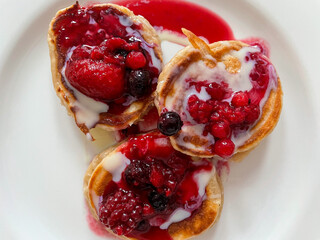 Homemade pancakes with fresh red berries and vanilla sauce on a white plate directly above view