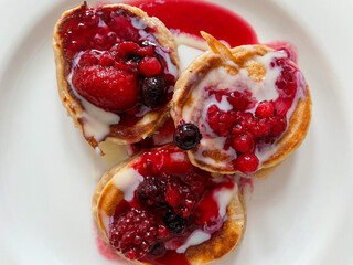 Homemade pancakes with fresh red berries and vanilla sauce on a white plate directly above view