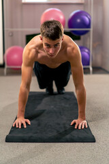 Fototapeta na wymiar young guy doing push-ups on the mat in the gym doing exercises for the muscles of the arms