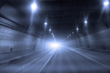 Tunnel with a bright light at the end, a car traveling down the road.