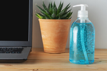 Hand sanitizer in a bottle on wooden table with a laptop. Coronavirus prevention concept.