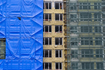 Building is under construction with blue tarps, external thermal insulation and scaffolding.