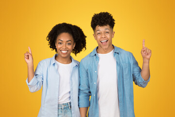 Happy and confident young woman and man with cheerful smiles pointing upwards