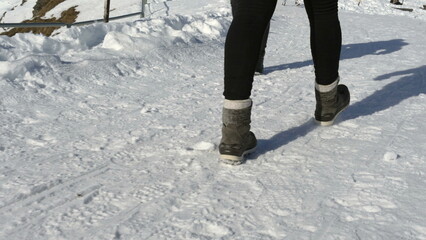 Closeup person walking in snow wearing boots, winter clothes - weather sealed footwear