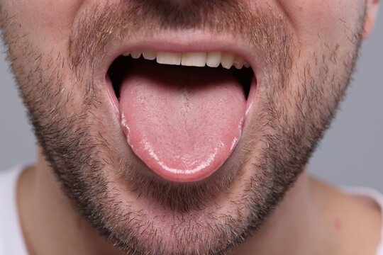Closeup view of man showing his tongue on grey background