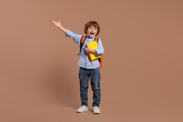 Emotional schoolboy with backpack and books on brown background
