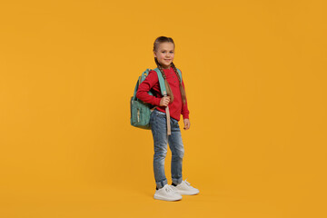Fototapeta premium Happy schoolgirl with backpack on orange background