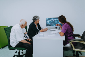An elderly couple engages in a thoughtful discussion with their dentist about modern denture...