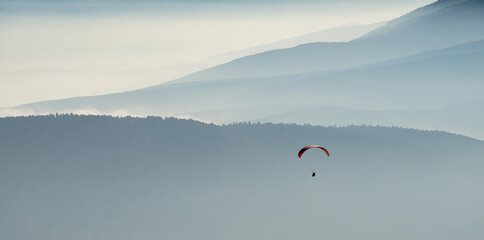 Paraglider in the air over mountains with sunrays coming over the hills at Hohe Wand in Lower...
