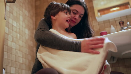 Nurturing scene of mother drying son after bath, bedtime night routine of nurturing mom taking care of her child seated inside bathroom. kid covered with towel receinv maternal affection