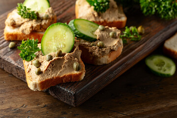  Open sandwiches with pate, cucumber, capers, and parsley on a old cutting board.