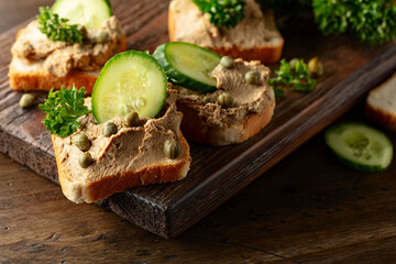 Open sandwiches with pate, cucumber, capers, and parsley on a old cutting board.