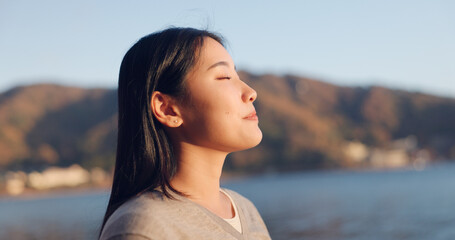 Japanese woman, breathing and peace outdoor, lake or ocean with travel, holiday and mindfulness in nature. Wellness, adventure and care free at beach in Japan, calm with freedom and positivity