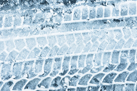 Snow tyre mark. Asphalt covered in snow. Dangerous road conditions. Car imprint on frozen ground. Tire trail on ice. City streets covered in snow during heavy snow fall. Slippery road background.