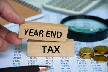 Year end tax text on wooden block with pen, notepad, calculator and coins background. Tax assessment concept - obrazy, fototapety, plakaty