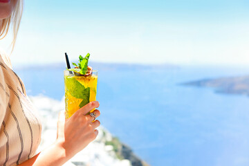 Woman holding a glass of passion fruit cocktail in Santorini background