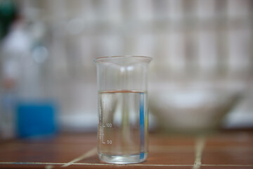 A measuring cup with a clear liquid standing on a tile