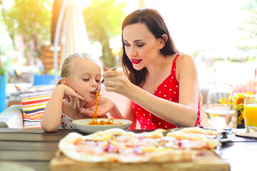 Happy mother and daughter eating spaghetti bolognese in the restaurant