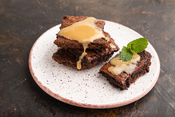 Chocolate brownie with caramel sauce with a cup of coffee on black concrete, side view.