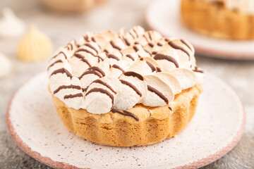 Two tartlets with meringue cream and cup of coffee on brown concrete, side view, selective focus.