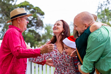 Happy Aussie family of multiple generations greeting one another with hugs at Christmastime