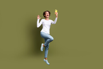 Fototapeta na wymiar Full size photo of attractive young woman jumping video call palm wave dressed stylish white clothes isolated on khaki color background