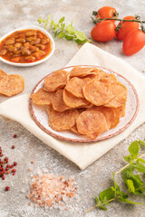 Slices of dehydrated salted meat chips on gray concrete, side view