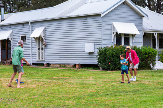 Young aussie boys playing backyard cricket with dad and grandfather in front yard of house - Powered by Adobe