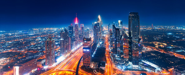 Night Panorama aerial top view of Dubai downtown skyscrapers with illuminated and highway. Business...